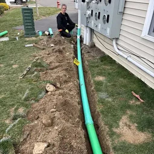 Trench beside a house with a green pipe laid in it, from the All Clear Sewer & Drain website